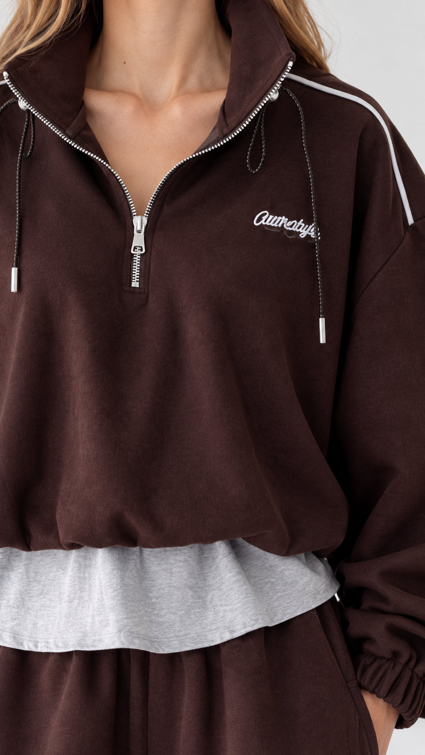 Close-up detail of half-zip collar, shoulder piping, and layered contrast hem