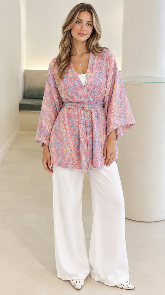 Front view of model wearing pink paisley print belted kimono cardigan with white wide-leg trousers