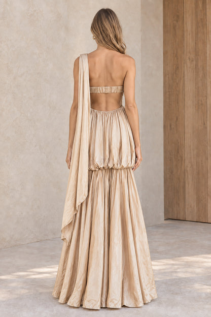 Back view of woman wearing champagne maxi dress highlighting cut-out back and draped shoulder detail