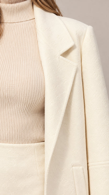 Close-up detail of cream lapel collar, ribbed mock-neck knit top, and fabric texture