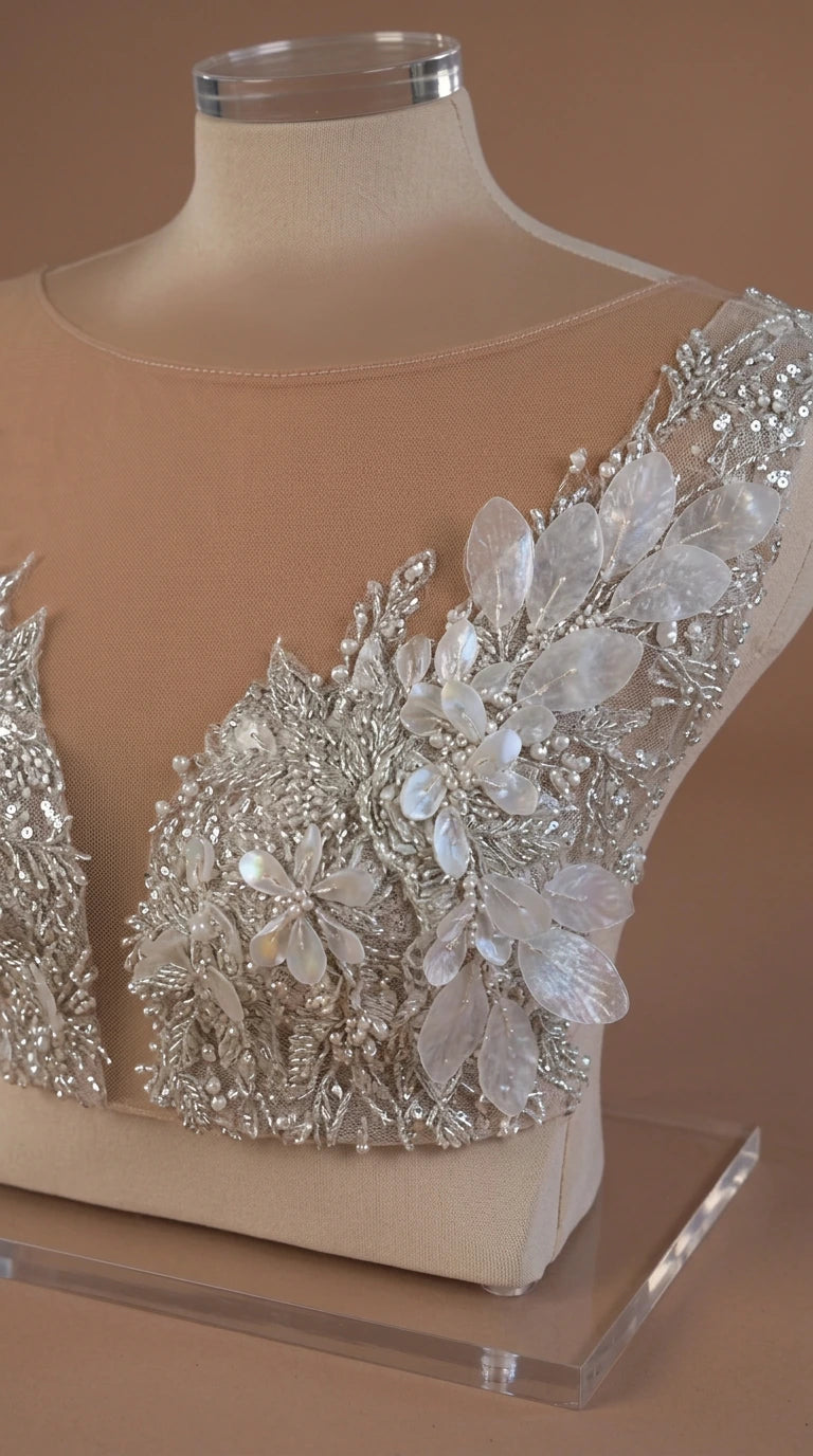 Close-up detail of sheer mesh neckline with intricate crystal beading and floral petal appliqués