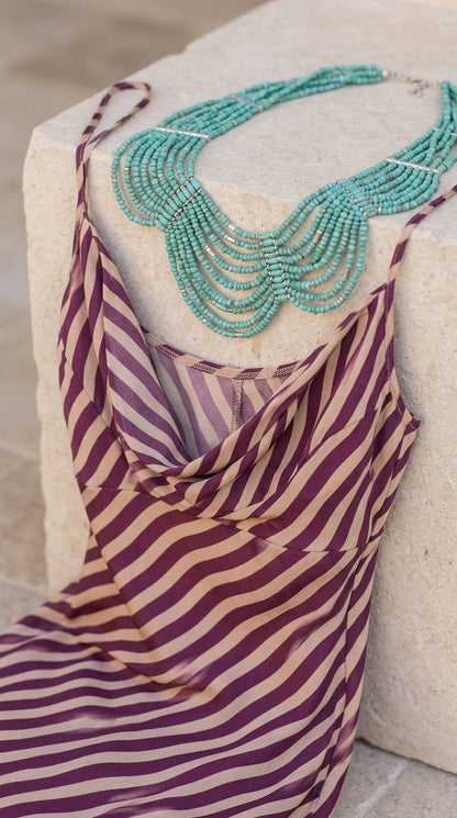 Close-up detail of draped cowl neckline and diagonal striped knit fabric with turquoise necklace