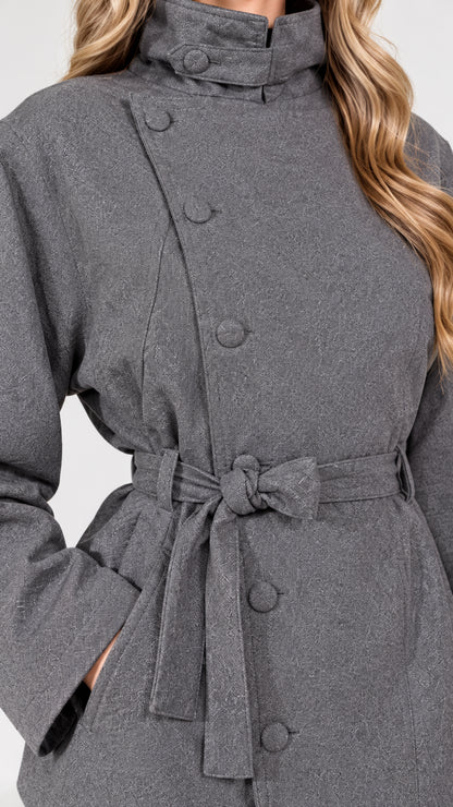 Close-up detail of grey jacket showing asymmetrical covered buttons and stand collar